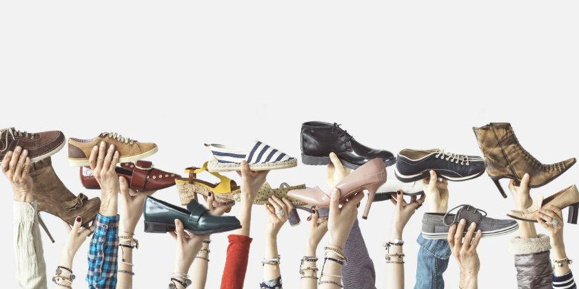 Muchos modelos de zapato distintos sostenidos en alto, de vestir, deportivos y de calle